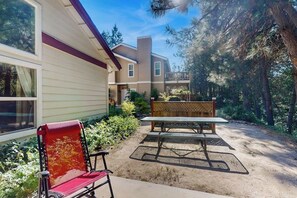 A patio area with a table and chairs, surrounded by a wooden fence and trees. - Creekside & Cozy - Pool, Fireplace & Dog-Friendly (Bass Lake)