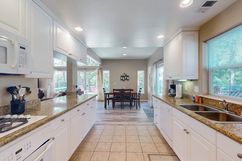 A kitchen with white cabinets, granite countertops, a dining table with chairs, and a window with blinds.