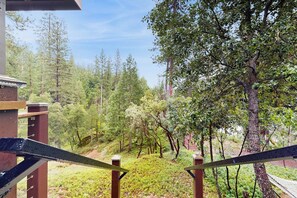 Blick vom Balkon mit Geländer auf eine bewaldete Landschaft mit Bäumen und einer Holzterrasse.