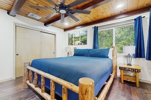 Ein Schlafzimmer mit einem hölzernen Bettgestell, einem Deckenventilator, einem Fenster mit Vorhängen und einem Nachttisch.