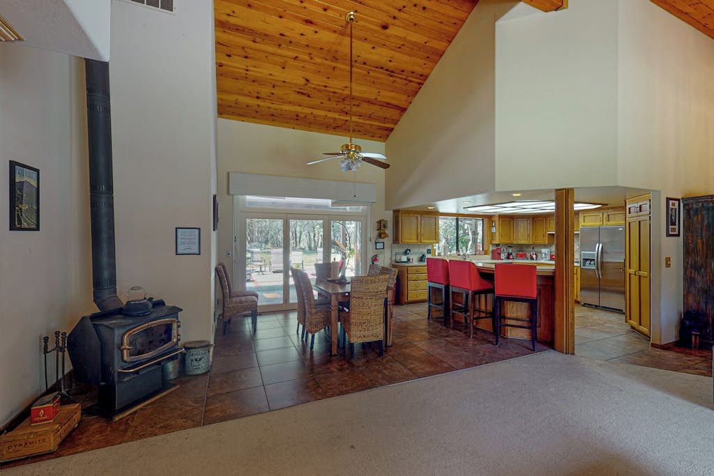 A spacious living area with a high ceiling, a fireplace, a dining table with chairs, and a kitchen area with cabinets and a refrigerator.