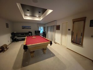 Ein Billardtisch in einem Raum mit einer Deckenleuchte, einer Tür und einem Fenster mit Vorhängen.