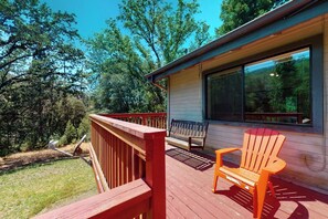 Eine Holzterrasse mit roter Geländer, einer hölzernen Bank und einem orangefarbenen Stuhl.
