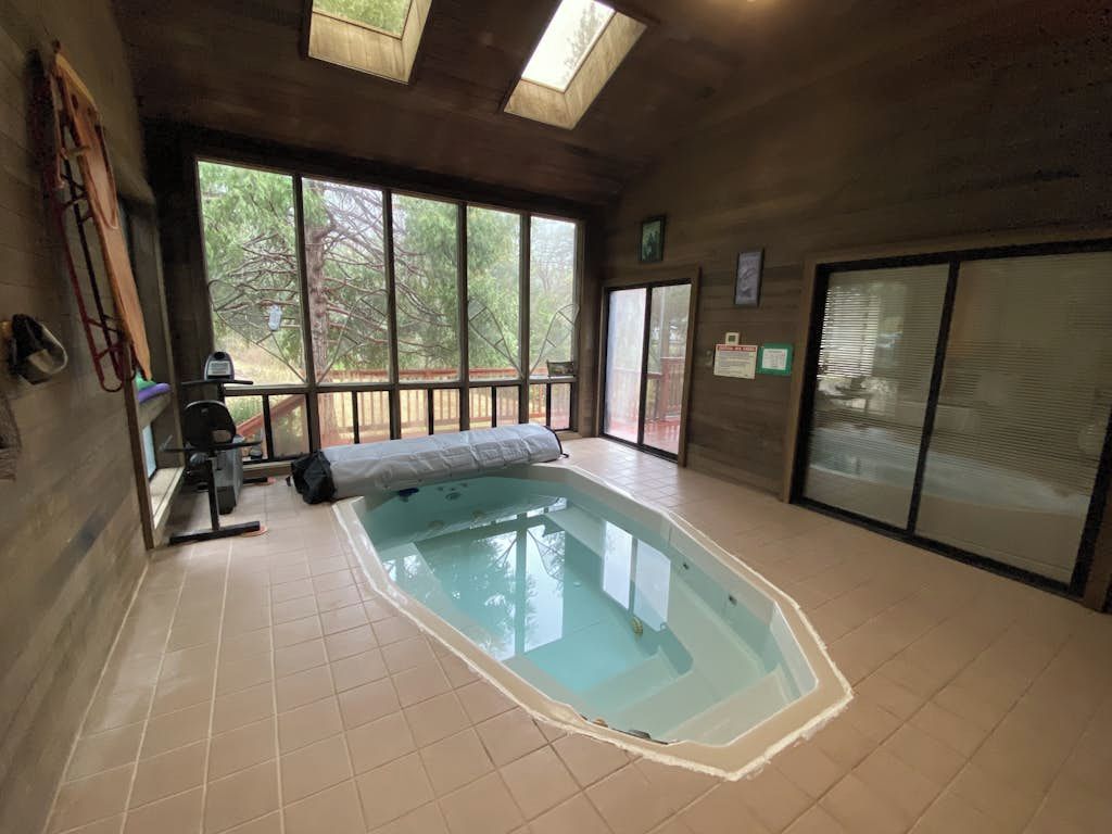 An indoor swimming pool with a tiled floor, a bench, and a window overlooking a tree.