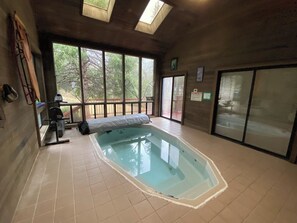 En inomhuspool med ett kaklat golv, en bänk och ett fönster med utsikt över ett träd.
