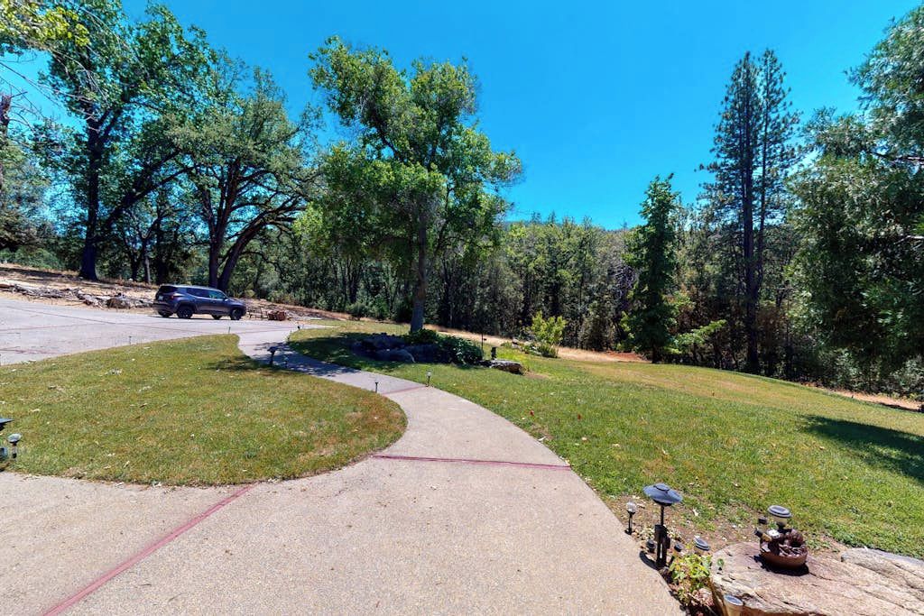 A residential driveway with a paved path, a parked car, and a lawn with a small garden area.