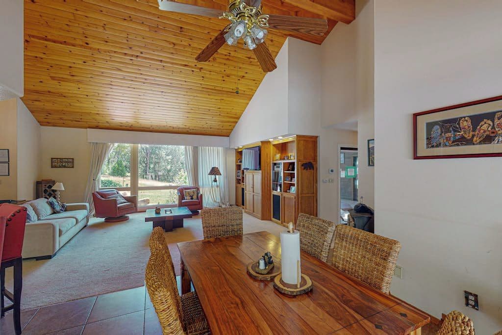 A spacious living area with a wooden ceiling, a dining table with chairs, and a bookshelf.