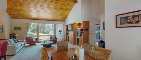 A spacious living area with a wooden ceiling, a dining table with chairs, and a bookshelf.