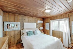 A wooden-paneled bedroom with a bed, bedside tables, a mirror, and a window with curtains. - Bear Den - Near Yosemite & Bass Lake, Deck (Oakhurst)