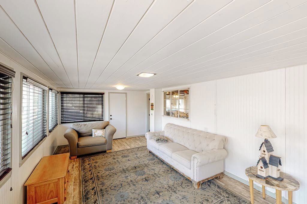 Et værelse med hvidt loft, en beige sofa, et mønstret tæppe og et lille bord med en lampe.