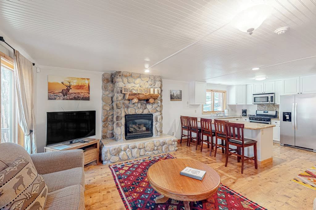 A living room with a stone fireplace, a television, a sofa, and a dining area with chairs and a table.