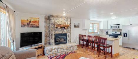A living room with a stone fireplace, a television, a sofa, and a dining area with chairs and a table.