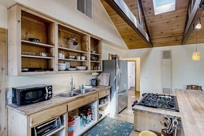 A compact kitchen with wooden shelves, a microwave, a refrigerator, and a gas stove.