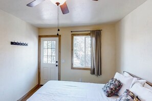A bedroom with a bed, a ceiling fan, a window with curtains, and a door.