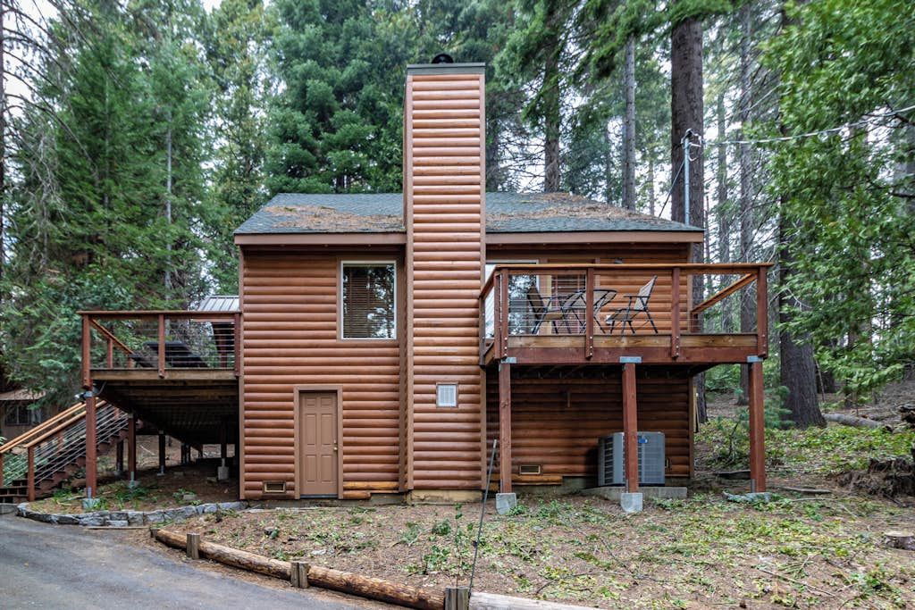 Una cabaña de madera con un balcón, una chimenea y una escalera que conduce a una terraza superior.
