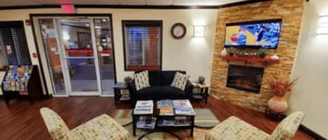 A lobby with a sofa, two armchairs, a coffee table, a fireplace, a television, and a clock on the wall.