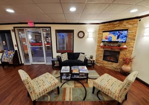 A lobby with a sofa, two armchairs, a coffee table, a fireplace, a television, and a clock on the wall.