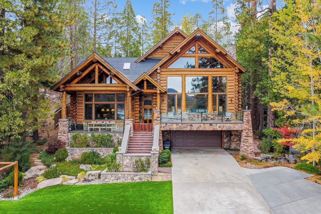 A log cabin with a stone foundation, large windows, and a covered patio.
