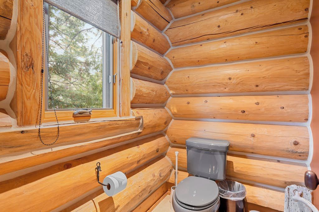 Interior d'una cabana de fusta amb un vàter, una finestra i una paret de fusta.