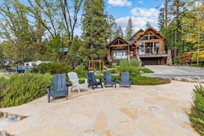 A log cabin with a stone patio, outdoor seating, and a garage. - Willow Cove Log Cabin (Bass Lake)
