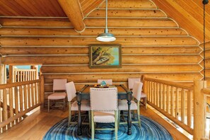 A wooden cabin interior with a dining table, chairs, a hanging light fixture, and a painting on the wall. - Willow Cove Log Cabin (Bass Lake)