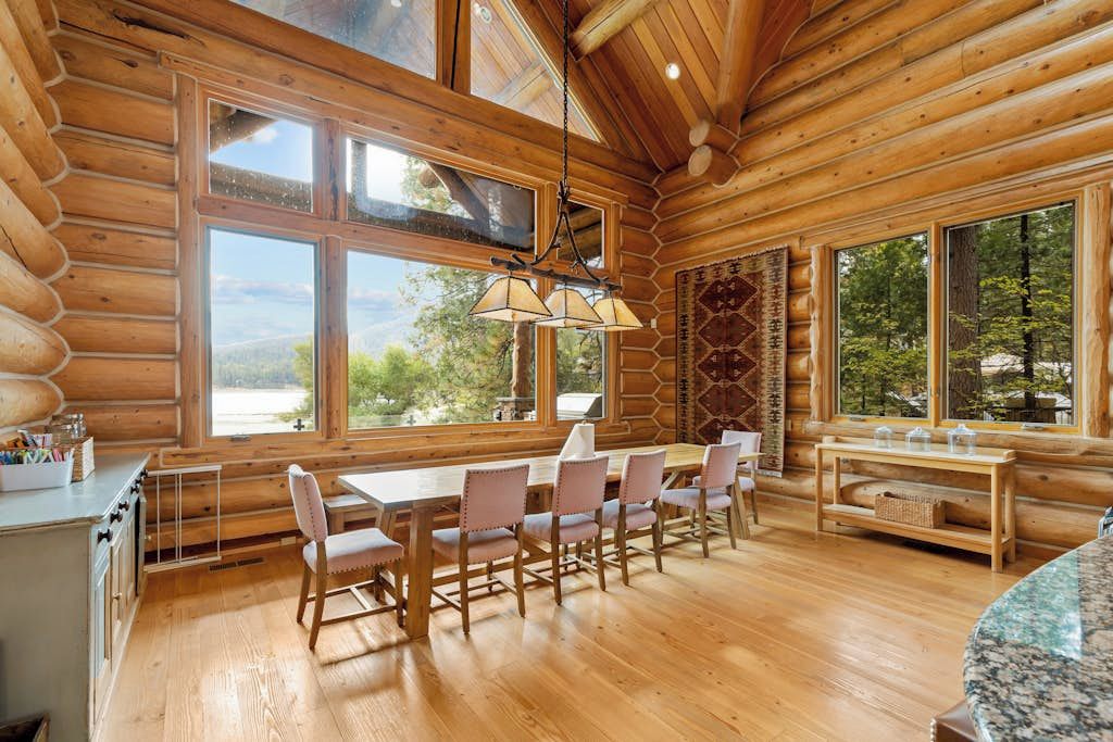 Interno di una baita di legno con zona pranzo, ampie finestre e vista sul paesaggio.