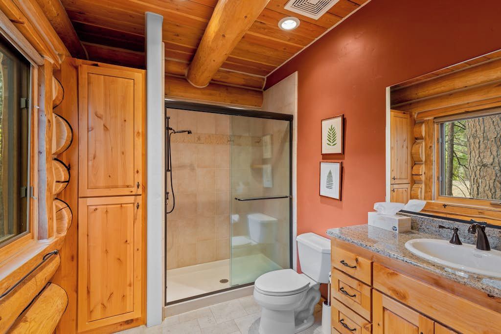 Une salle de bain rustique, avec des murs en bois, une douche en verre, des toilettes blanches et un meuble-lavabo avec un miroir.