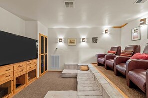 A living room with a large flat-screen TV, leather sofas, a sectional sofa, and wall-mounted lighting. - Willow Cove Log Cabin (Bass Lake)