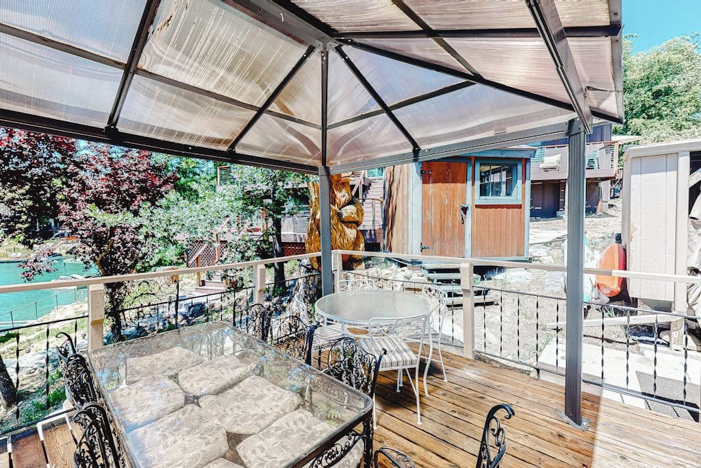 A covered outdoor patio with a glass table and chairs, surrounded by a wooden deck and metal railings.