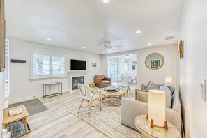 A spacious living room with a fireplace, comfortable seating, and a large window. - Slide Creek Retreat - Pool, Hot Tub, Walk to Lake (Bass Lake)