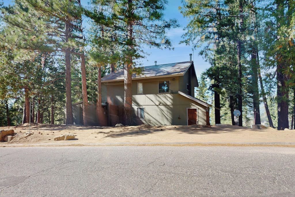 Une maison à deux étages avec un garage, entourée de grands pins.