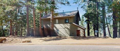 A two-story house with a garage, surrounded by tall pine trees.