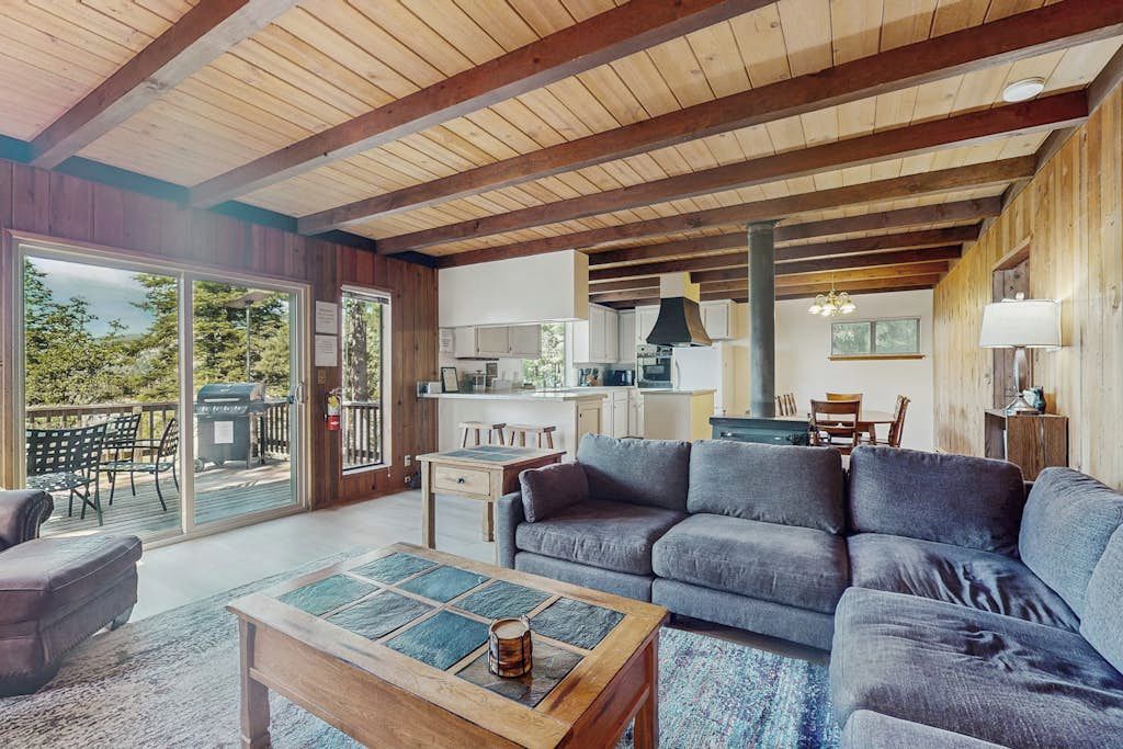 A spacious living area with a large sofa, a coffee table, and a view of the kitchen through a glass door.