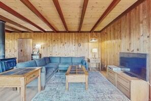 Ein Zimmer mit Holzwänden, einer Couch, einem Couchtisch, einem Fernseher und einem Kamin.