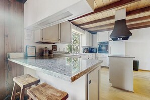 A kitchen with a granite countertop, wooden stools, white cabinets, and a black range hood. - Vernal Vista - Inside Yosemite, Deck & Views (Yosemite West)