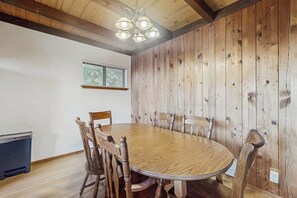 Ein Essbereich mit einem runden Holztisch und Stühlen, einer Deckenleuchte und einem Fenster mit Jalousien.