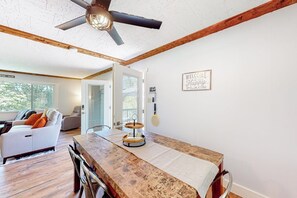 Sala de estar moderna com mesa de jantar de madeira, ventilador de teto e vista para o exterior.