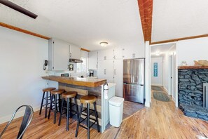 Cozinha moderna com ilha central, banquetas, geladeira e parede de pedra.