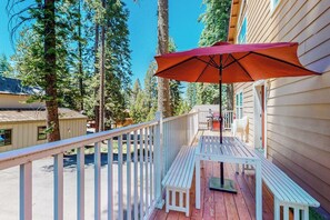 A wooden deck with a white railing, a red umbrella, and a bench.