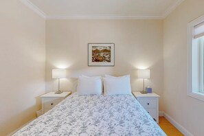 A bedroom with a bed, two bedside tables, a nightstand, a wall-mounted picture, and a window.