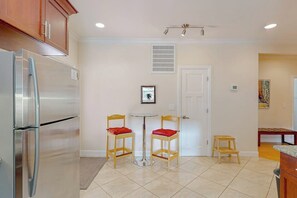 A kitchen with a stainless steel refrigerator, two wooden chairs with red cushions, a small round table, and a white door.