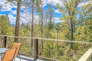 A balcony with a table and chairs overlooking a forested area. - Alford Family Lodge - Walk to Bass Lake, 2 Decks (Bass Lake)
