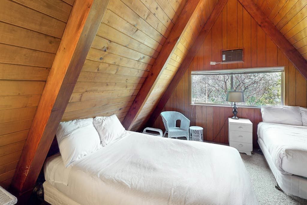 A cozy attic bedroom with a sloped ceiling, a window with a view, a bedside table, a chair, and a bed.