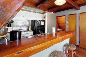 A kitchen with a wooden bar counter, white cabinets, a black refrigerator, and a stove. - Alford Family Lodge - Walk to Bass Lake, 2 Decks (Bass Lake)