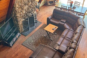 A cozy living room with a stone fireplace, leather sofa, and a coffee table. - Alford Family Lodge - Walk to Bass Lake, 2 Decks (Bass Lake)