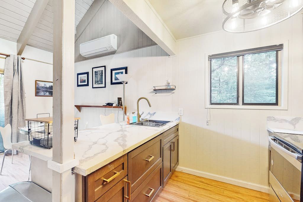 A modern kitchen with a marble countertop, wooden cabinets, and a window with a view of trees.