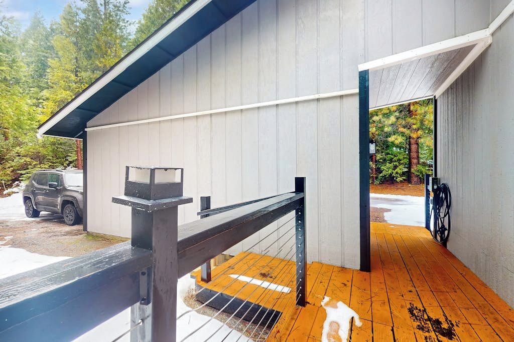 Un espace extérieur abrité doté d’une terrasse en bois, d’une rambarde en métal et d’un véhicule garé à l’extérieur.