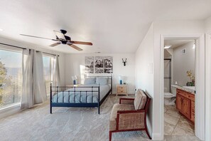 Un dormitorio con cama, una silla, un ventilador de techo, una mesita de noche y un adorno de cabeza de venado montado en la pared.