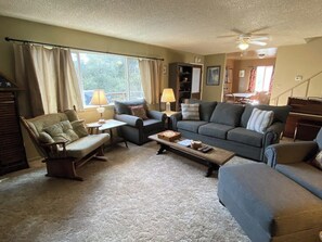 A living room with a sofa, armchair, coffee table, and a bookshelf. - Hodges Hill Yosemite House (Oakhurst)