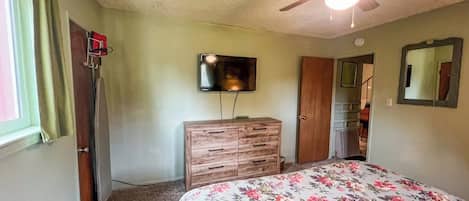 A bedroom with a bed, a ceiling fan, a dresser, a television, and a door leading to another room.
